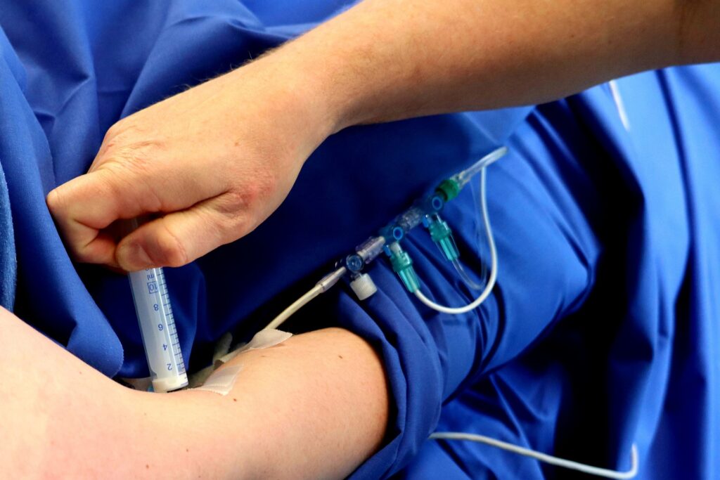 A syringe is injected into a patient's arm via a braided flexible tube structure.