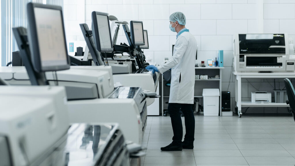 A man in a white lab coat studies a computer monitor in a white, clean laboratory.